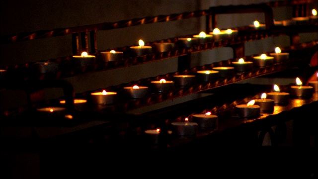 在黑暗的大教堂里，一排排点燃的蜡烛摇曳着。视频下载