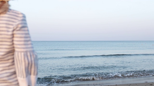 海边的日出。清晨，一位戴着草帽的老妇人站在海滩上。视频素材