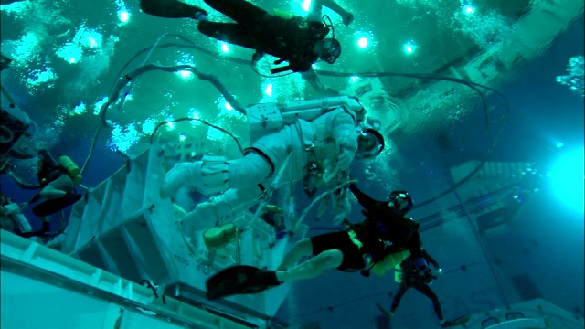 潜水员在中性浮力实验室里把宇航员带到水下。视频素材