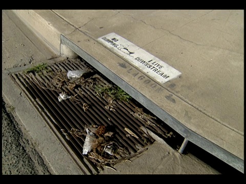 垃圾覆盖了路边的一个格栅，旁边是一只鸭子的标志和“禁止倾倒”和“我住在下游”的字样。视频下载