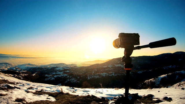 日落背景上三脚架上的无反光镜相机剪影。在日落时拍摄乡村风景视频素材