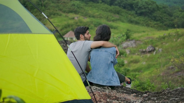 一对年轻夫妇坐在山上露营旅行的帐篷前。视频素材