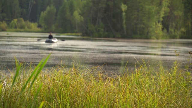 渔夫乘着充气船在河回水里游泳。周末的爱好。平静的夏天的风景。夏天闷热的中午，在森林湖岸边。4 k的视频视频素材