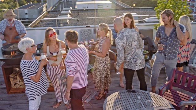 城市屋顶烧烤- 20个时尚，时尚和多元文化的人享受一个聚会在屋顶平台上，而阳光明媚的夏日和一个漂亮的女人出现了一碗海鲜。视频下载