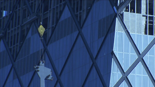 工人们看着吊车将一段金属部件吊向CCTV大楼的顶部。视频下载
