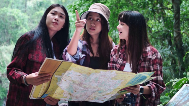 一群朋友十几岁的亚洲女性在森林里互相帮助找到旅行方向地图视图。冒险假期。视频下载