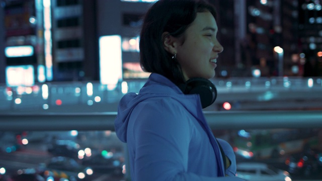 日本东京，一名年轻女子戴上帽衫和耳机，微笑着伸展身体视频下载