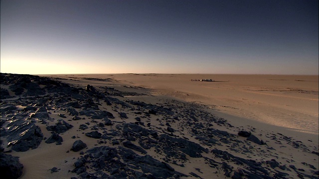 一个沙漠营地坐落在岩石沙丘的一侧。视频下载