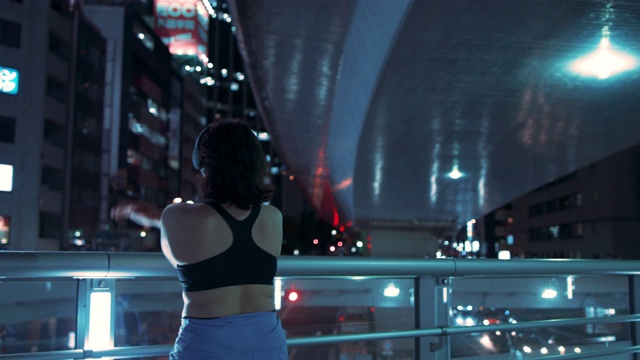 年轻女子在运动胸罩伸展在夜晚的桥梁在东京，日本视频下载
