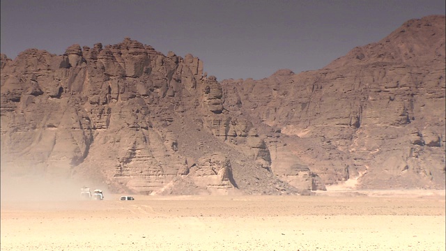 在Gilf Kebir，越野车驶过巨大的岩层时扬起了尘土。视频下载