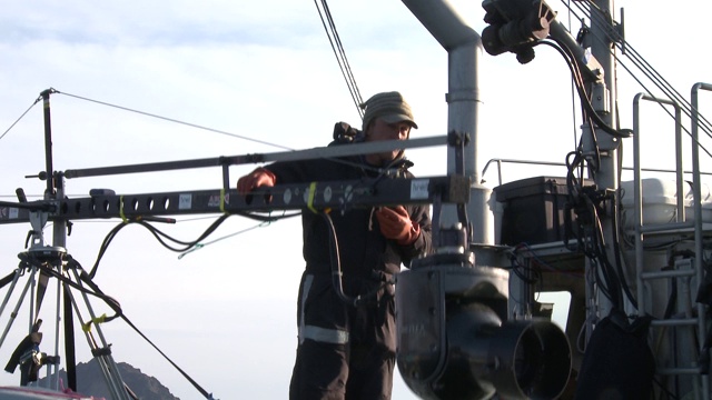 一名船员在船上的吊杆上升降一个摄像机。视频下载