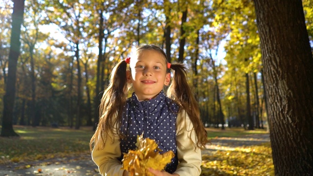 一个小女孩在秋天的公园里跳着，扔着黄叶视频素材