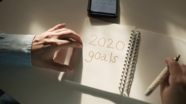 近距离的女人手写的2020年新年目标在书桌上的笔记本和从窗户的阳光视频素材