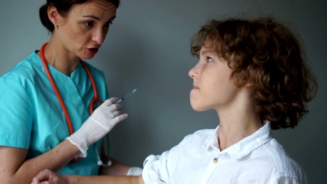 医生助理给一个卷发男孩打预防针。流感疫苗，免疫计划。医疗保健理念视频素材