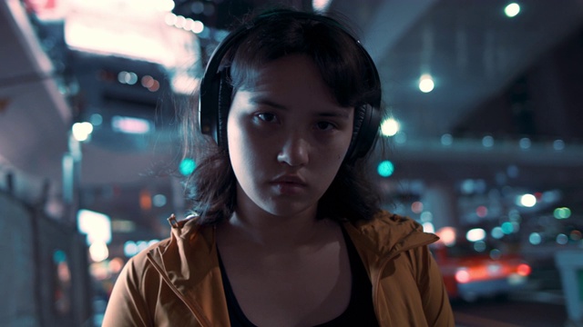 在日本东京，一个年轻的日本女人在晚上戴着耳机视频下载