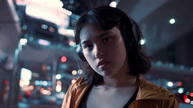 在日本东京，一个年轻的日本女人在晚上戴着耳机视频下载