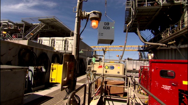 在海上钻井设施，起重机将一个金属盒子吊下来。视频下载