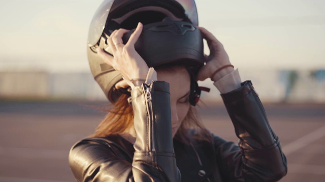 漂亮的年轻红发女摩托车手，戴着黑色摩托车头盔。骑摩托车的女孩脱下了她的头盔视频下载