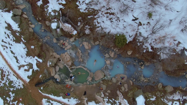 无人机徒步者在冬天的风景中，在热绿松石池中享受治疗浴视频素材