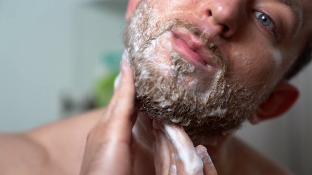 男子的手在剃须膏上按摩的特写镜头。男模特的肖像，脸上涂了剃须膏。用泡沫剃须、日常卫生和皮肤护理视频素材