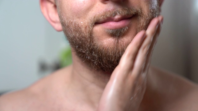 时髦男子把理发师的洗发水倒在手上，然后涂在他干燥的胡子上。英俊男子在剃须前清洁面部毛发。男士胡须上的洗发泡沫，修剪胡须前的准备工作。护肤和男子气概的概念视频下载