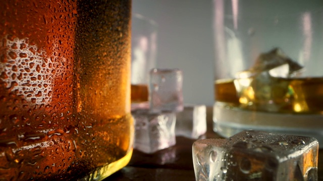 威士忌酒瓶和玻璃杯中加入冰块。特写镜头多莉拍摄视频素材