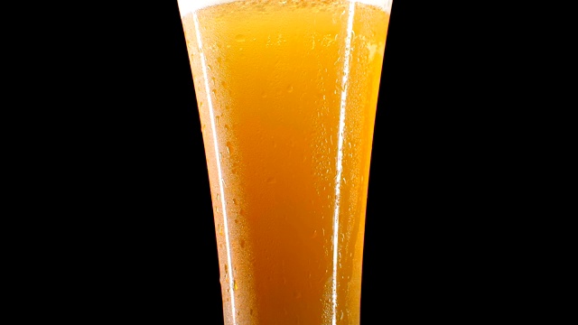 特写慢镜头:在黑色的背景上，冰镇啤酒倒进一个大滴啤酒和泡沫的玻璃杯。视频素材