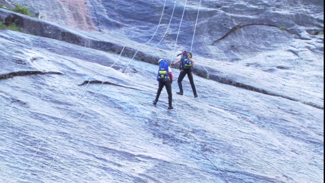 团队攀岩者在其他队员的注视下一起从悬崖上滑下来。视频素材
