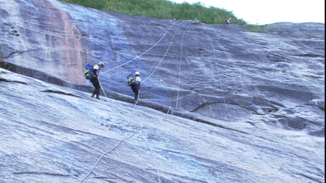 登山队从光滑的岩石表面攀爬而下。视频素材