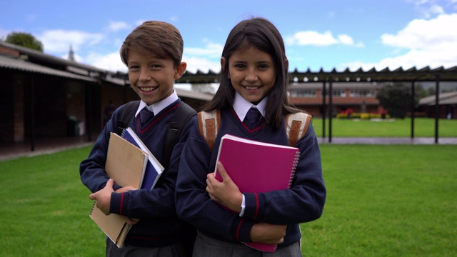 朋友们带着他们的笔记本和背包站在学校操场上，对着相机微笑视频下载