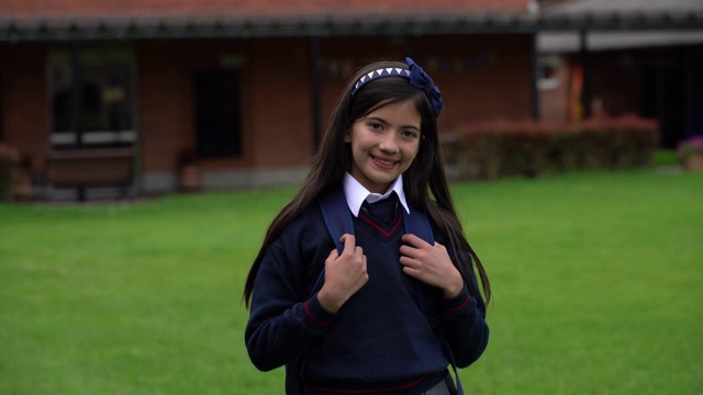 快乐的女孩在学校看着相机微笑，而拿着她的背包背带-教育概念视频下载
