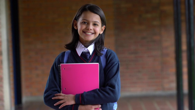 美丽的女孩在她的学校操场上拿着笔记本，对着相机微笑视频下载