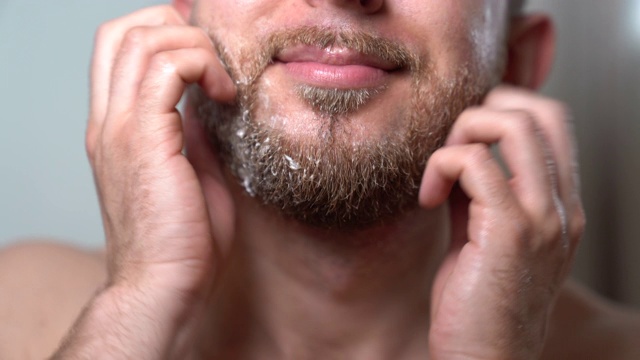 男人早晨在镜子前做面部手术的特写镜头。在家护理皮肤和剃须卫生。男人倒剃须香波和制造泡沫。准备刮胡子的野蛮男人。电动剃须器视频素材