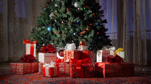 晚上在房间里装饰圣诞树。令人惊奇的闪烁的花环放射圣诞精神和心情。暗室与圣诞和新年室内装饰。圣诞树装饰着圣诞礼物盒和玩具视频素材