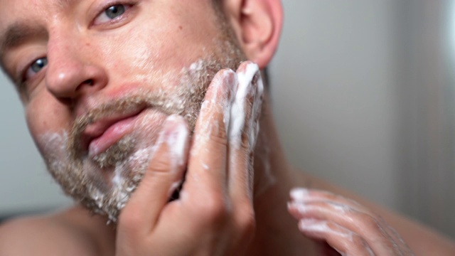 年轻英俊的男子用理发店特制的剃须香波擦洗他未剃的胡子。早上例行野蛮男人在浴室，皮肤护理和胡须卫生，特别男性面部毛发治疗在家。时尚剃胡子视频素材