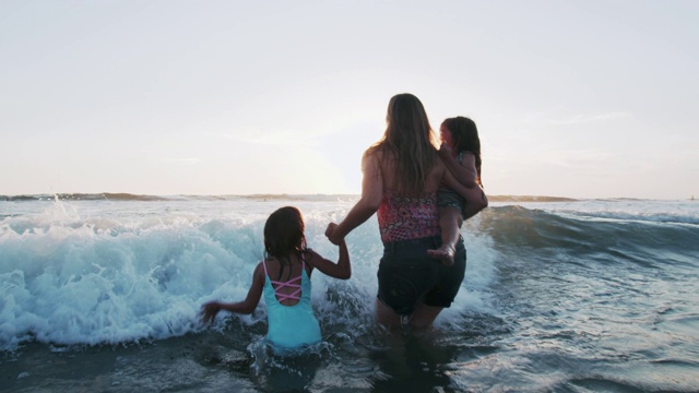 母亲和女儿在海浪中嬉戏视频素材