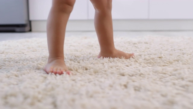 蹒跚学步的孩子光着腿在地毯上走路视频下载