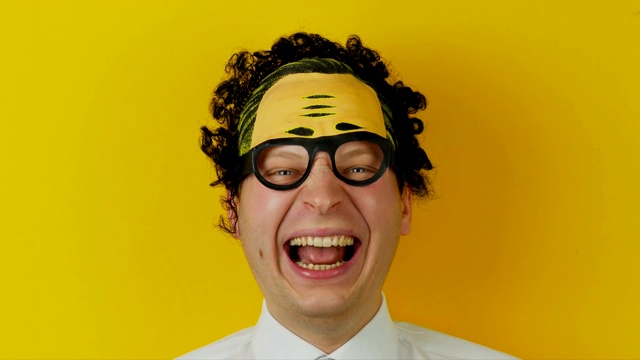 黄色的墙壁背景上，一个年轻的卷毛笑着的男人的肖像，有趣而愉快的人类情感视频下载