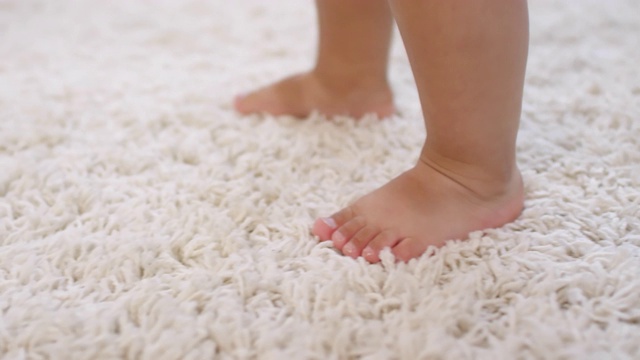 在地毯上学习走路的不知名的赤脚幼儿的腿视频下载