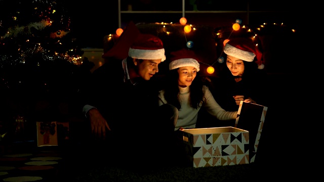 圣诞快乐!圣诞节时，微笑的孩子和她的父母正在打开一个装有闪亮爆炸光的礼盒视频素材