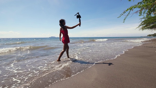 旅行女视频博主走在沙滩上，用单反相机录制视频。视频下载