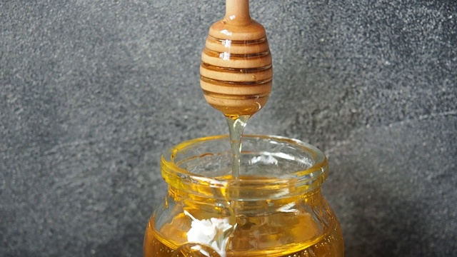 金色的液体蜂蜜从棍子流进一个玻璃罐视频素材