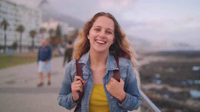一个微笑的金发年轻女人的肖像站在城市街道与她的背包看相机视频素材