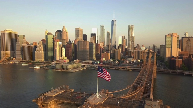航拍:在布鲁克林大桥上向后飞行，曼哈顿日出/日落时近距离看到美国国旗(4K)视频素材
