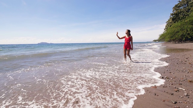 一名身穿红裙的旅游视频博主在海边拍摄视频博客。视频素材
