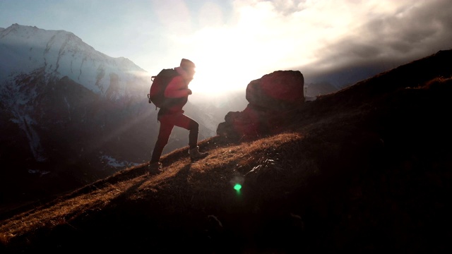 鸟瞰图的史诗镜头的一个女孩走在山的边缘作为一个剪影在美丽的日落。一个戴着帽子背着背包爬山的女孩的剪影视频下载
