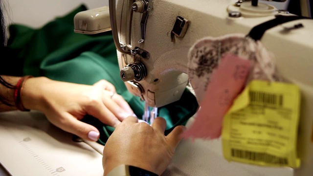 一个年轻女子的手与缝制绿色织物与缝纫机的特写。女人的手在缝纫机上缝东西。时尚、创作和剪裁。高角度视图视频素材