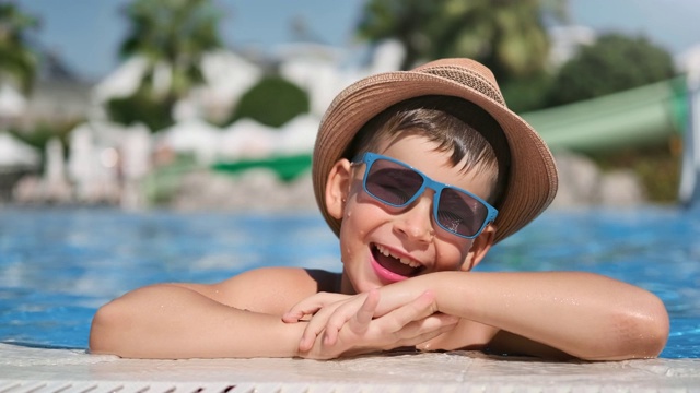 快乐男孩的肖像戴太阳镜和帽子摆姿势在游泳池有乐趣的特写视频素材