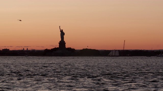 日落时自由女神像的剪影，前景是一艘帆船视频下载