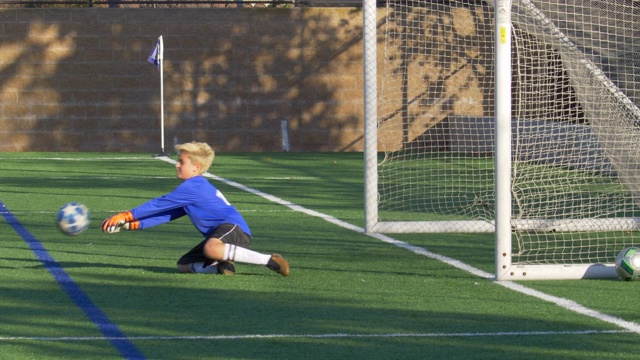 在一个草坪上，一个男孩在少年足球比赛中救了一个球。——慢动作视频下载